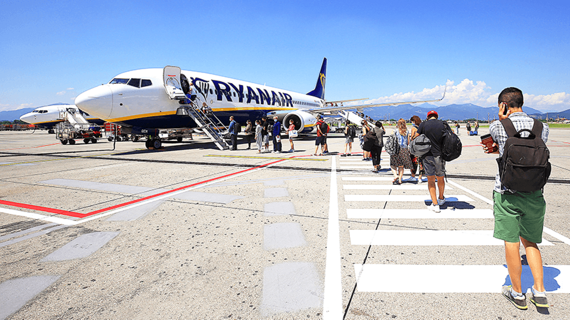 Cestujúci s príručnou batožinou kráčajú po odbavovacej ploche k lietadlu Ryanairu