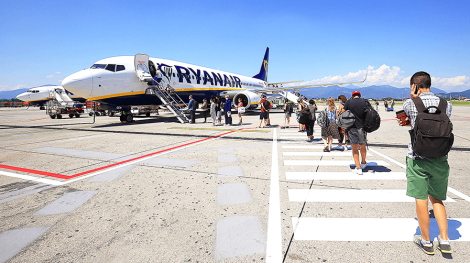 Cestujúci s príručnou batožinou kráčajú po odbavovacej ploche k lietadlu Ryanairu