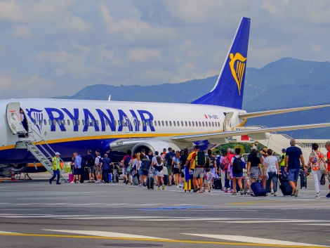 Cestujúci s kuframi nastupujú po schodíkoch do lietadla Ryanair na odbavovacej ploche letiska