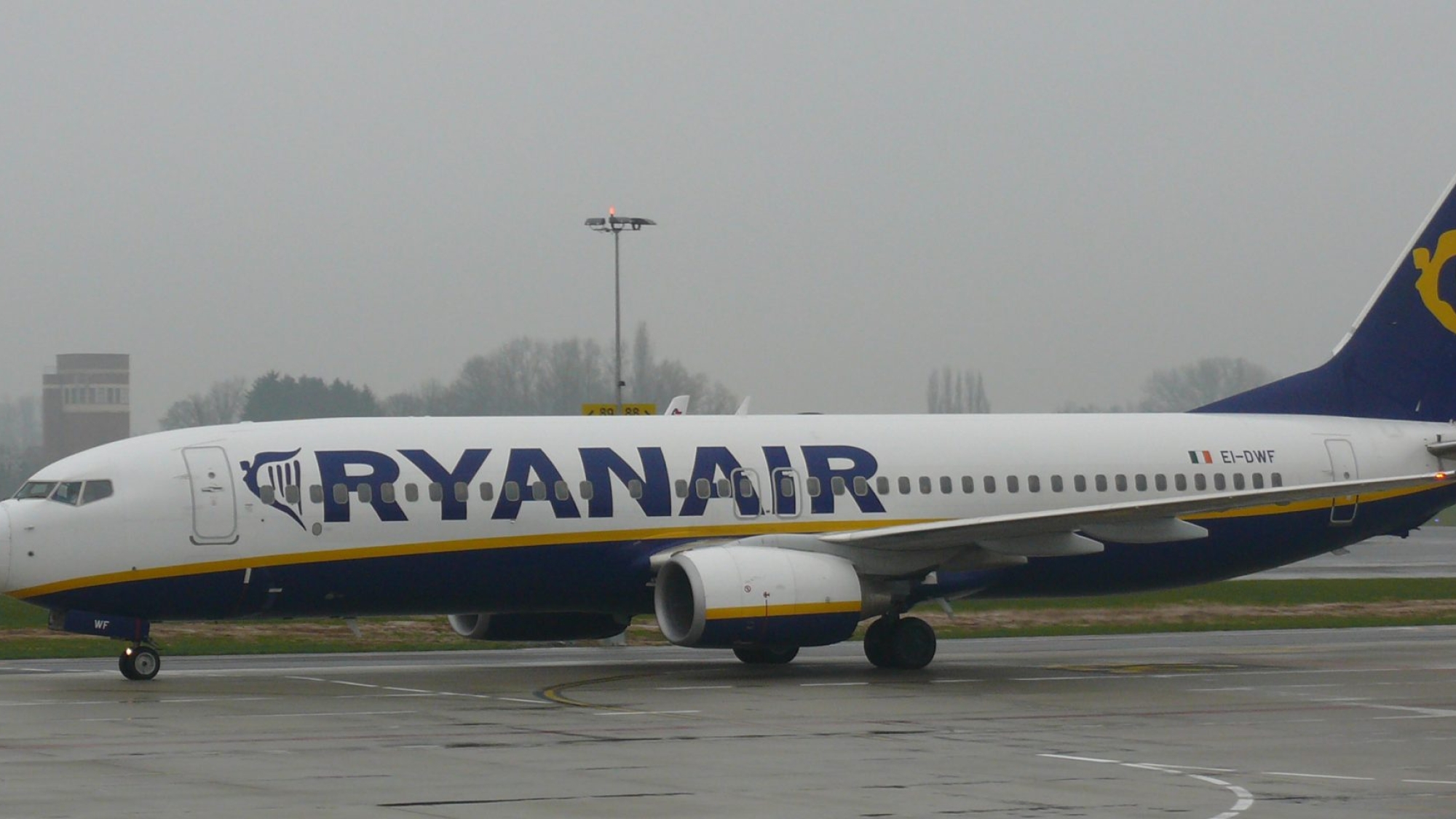 Boeing 737-800 v modro-žltých farbách Ryanairu roluje po mokrej odbavovacej ploche letiska pod zamračenou oblohou